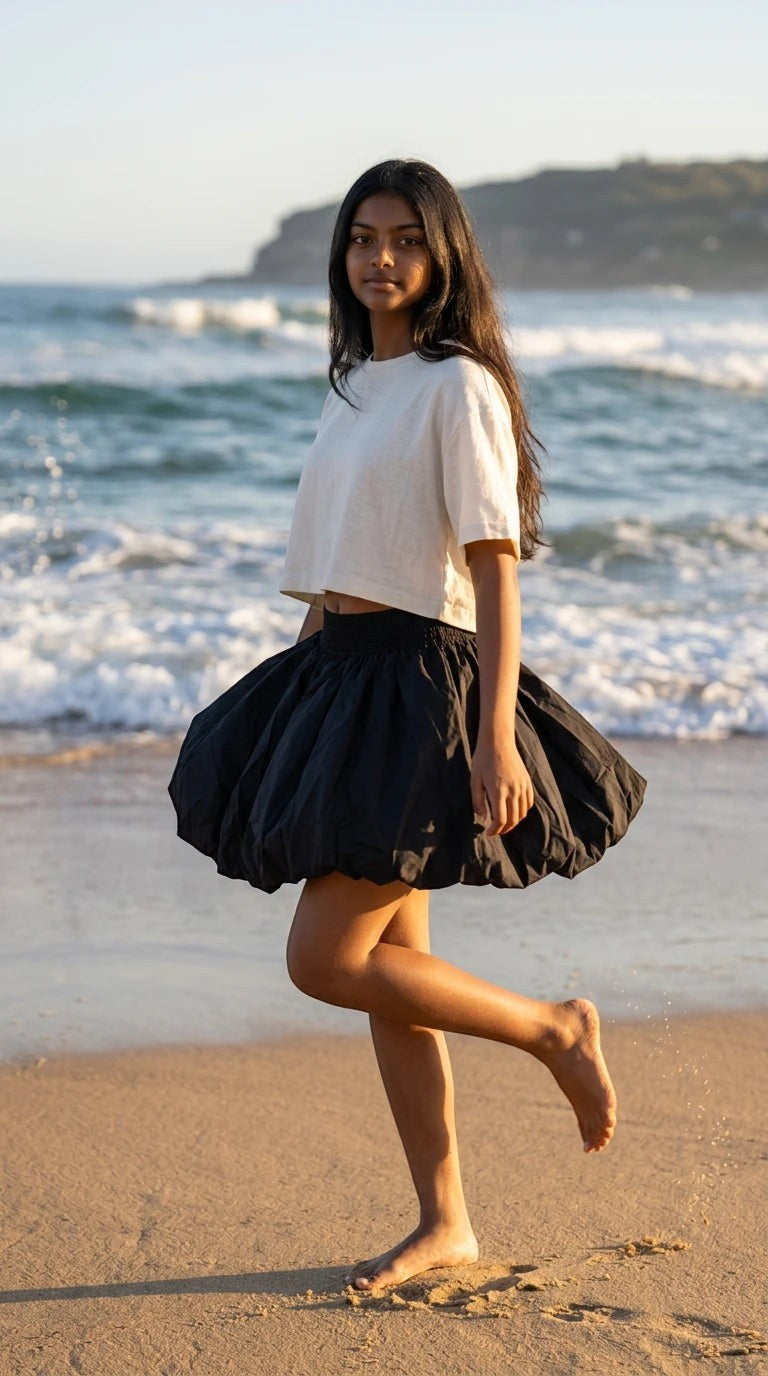 Luxury Clique black bubble mini skirt with elastic waist worn by a woman on a sunny beach with a white crop top