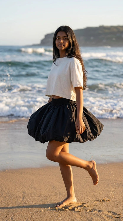 Luxury Clique black bubble mini skirt with elastic waist worn by a woman on a sunny beach with a white crop top