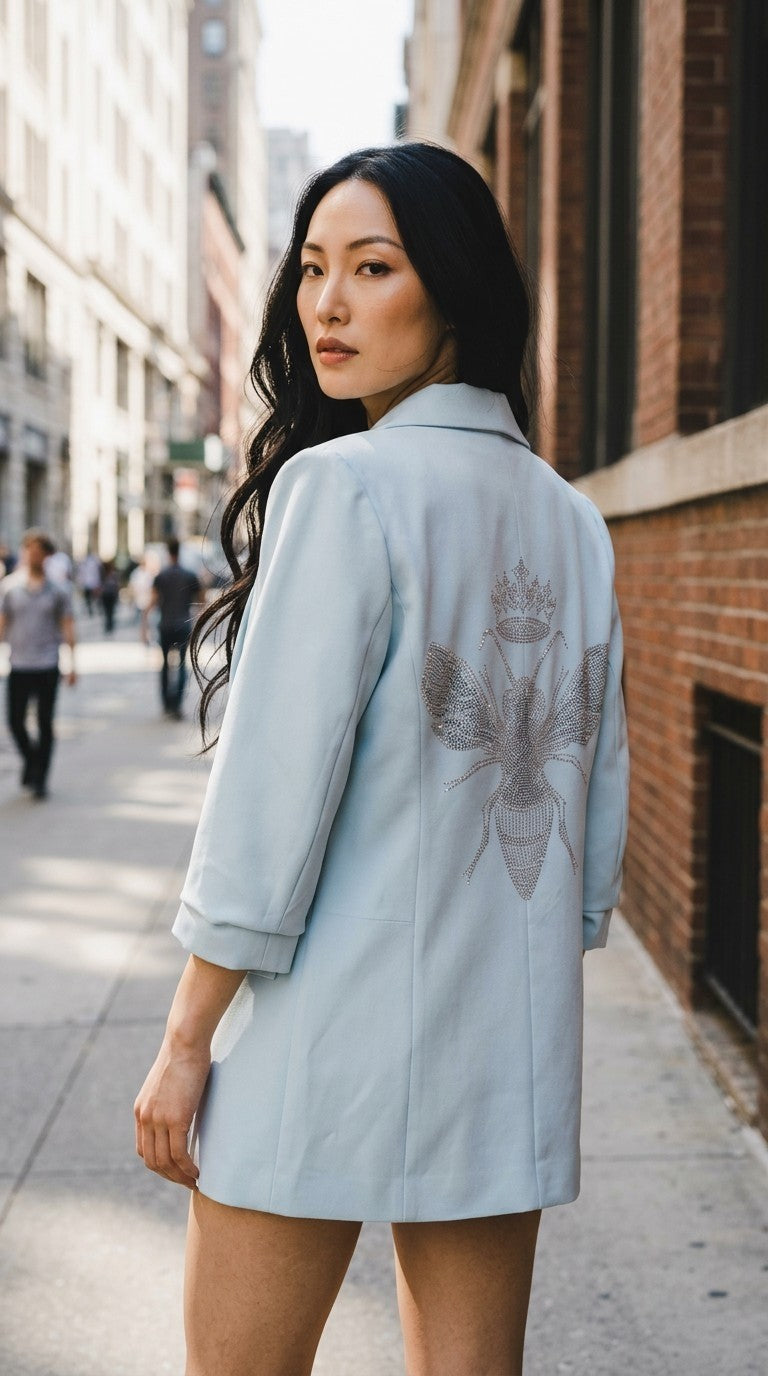Luxury Clique light blue tailored blazer with a sparkling sequin bee motif on the back, worn by a woman outdoors.
