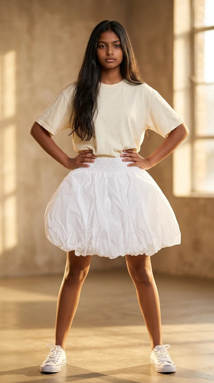 Luxury Clique white high-waisted bubble mini skirt with a smocked waistband worn by a model with a cream t-shirt.