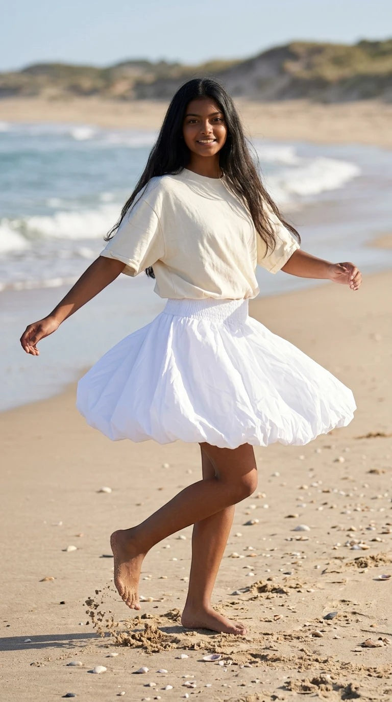 Luxury Clique white high-waisted bubble mini skirt with a smocked waistband worn by a woman on a sandy beach.